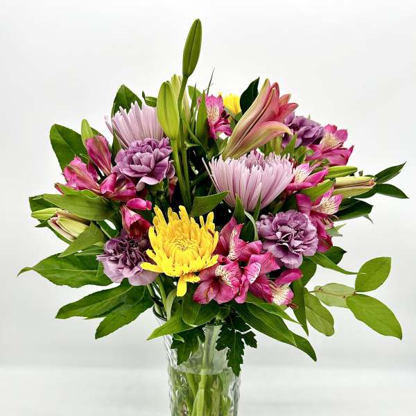 Mixed pink, purple, and yellow flowers in a clear glass vase