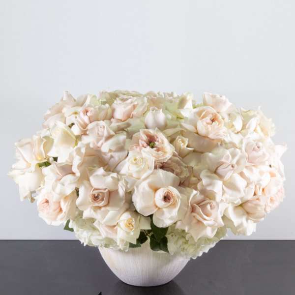 Low arrangement of ivory and blush roses densely packed in a white ceramic bowl
