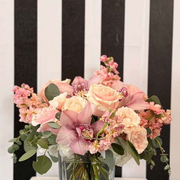 Pink roses and orchids arranged in a clear square vase.