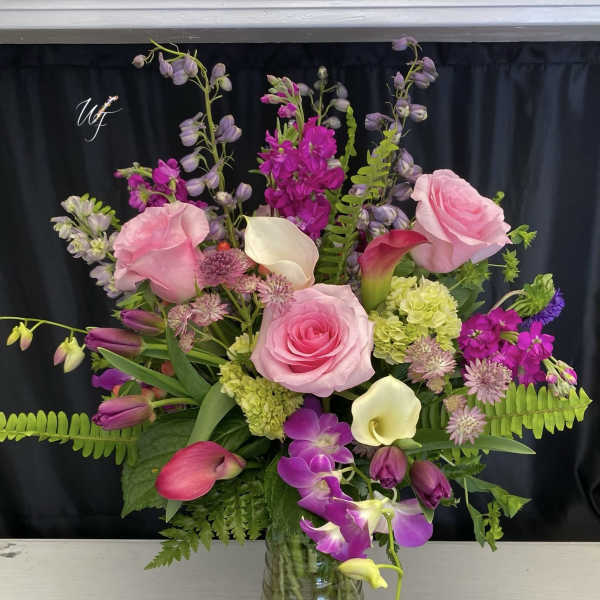 Pink roses and purple orchids arranged in a glass vase