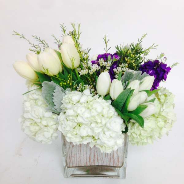 White tulips and hydrangeas in a clear square vase with purple flowers
