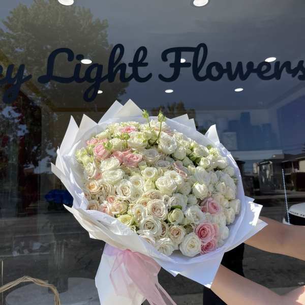 Large bouquet of white and blush roses wrapped in white paper with a pink ribbon