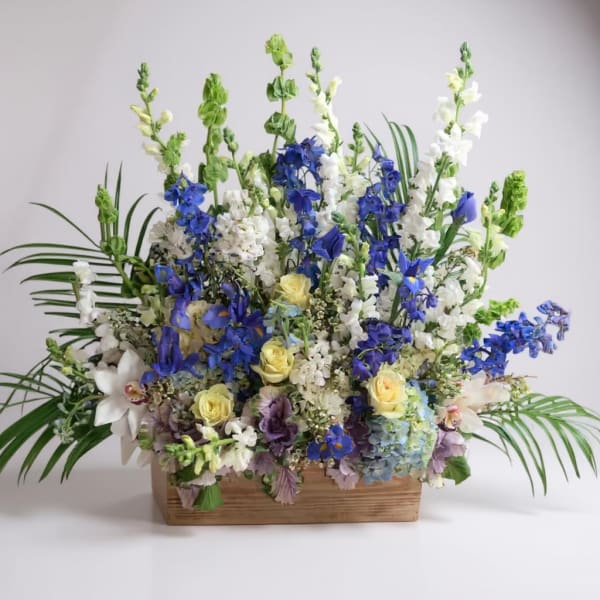 Tall floral arrangement with blue, white, and yellow blooms in a wooden box