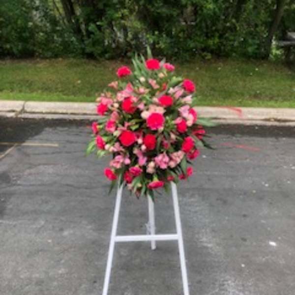 Standing floral wreath of pink and red flowers on a white easel