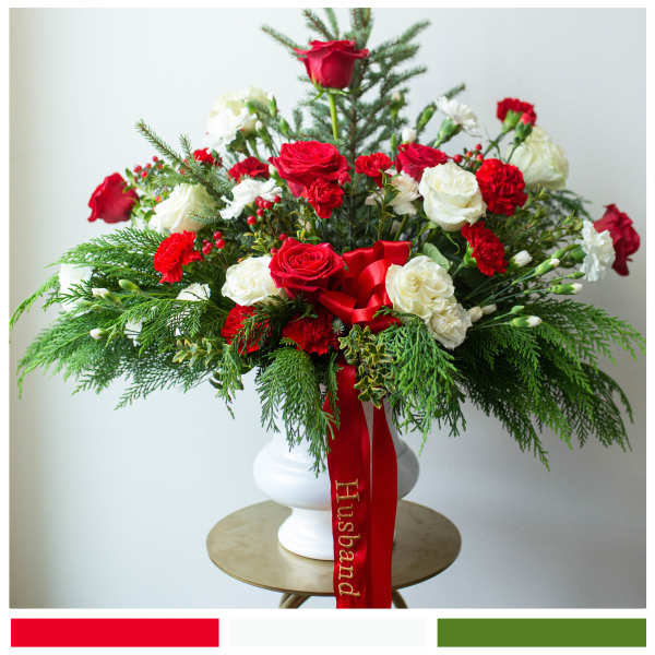 Red and white rose arrangement in a white vase with a red ribbon