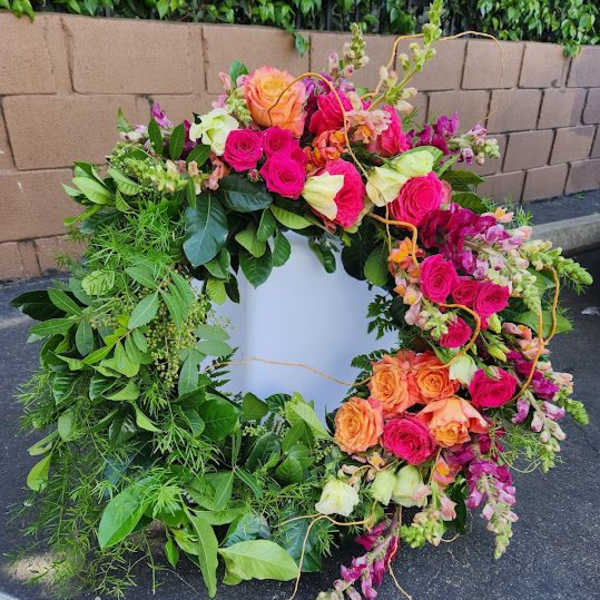 Large green wreath with bright pink and orange roses and accent flowers on one side