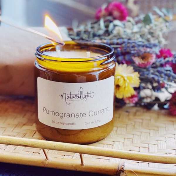 Amber glass jar pomegranate currant candle being lit on a woven tray with dried flowers behind