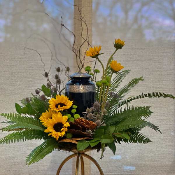 Yellow sunflowers arranged around a dark urn with ferns and branches