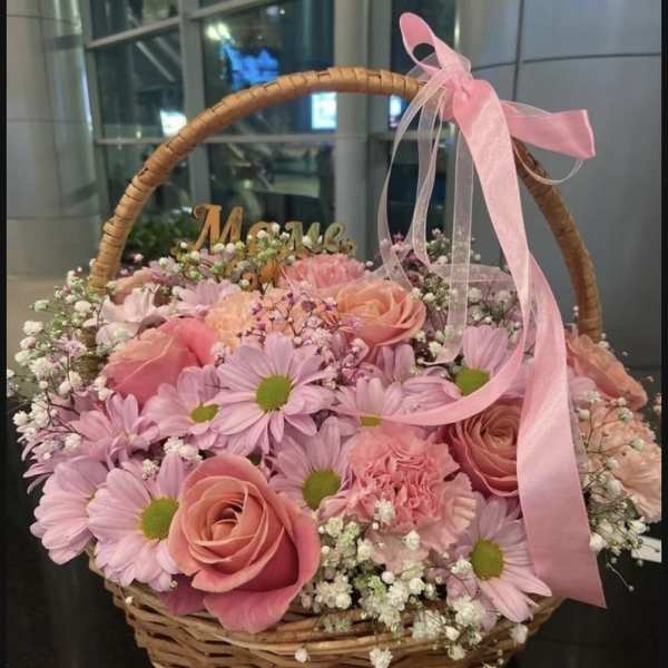 Pink roses and daisies arranged in a wicker basket with a pink ribbon