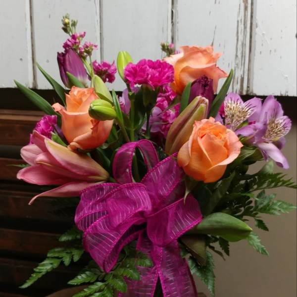 Bouquet of orange roses, pink lilies, and purple flowers with a magenta ribbon