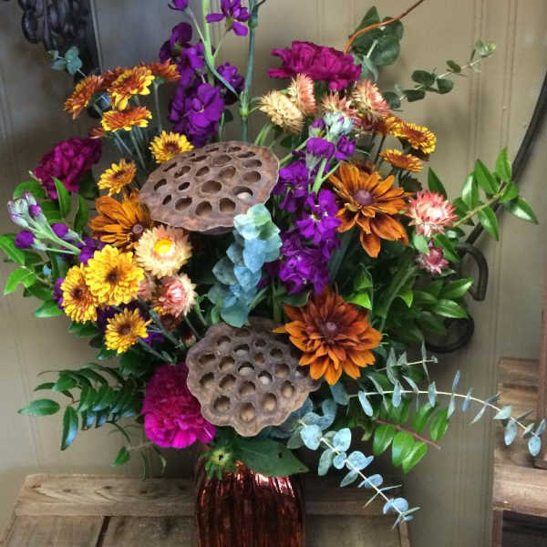 Tall mixed bouquet with purple, orange, and yellow flowers in a red vase