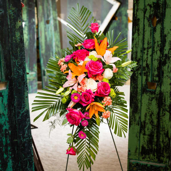 Standing floral spray with pink roses, lilies, and palm fronds