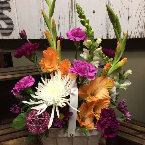 Colorful mixed flower arrangement in a white basket with a ribbon