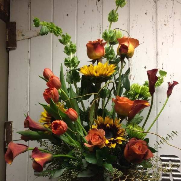 Mixed bouquet with orange roses, calla lilies, and sunflowers in a vase