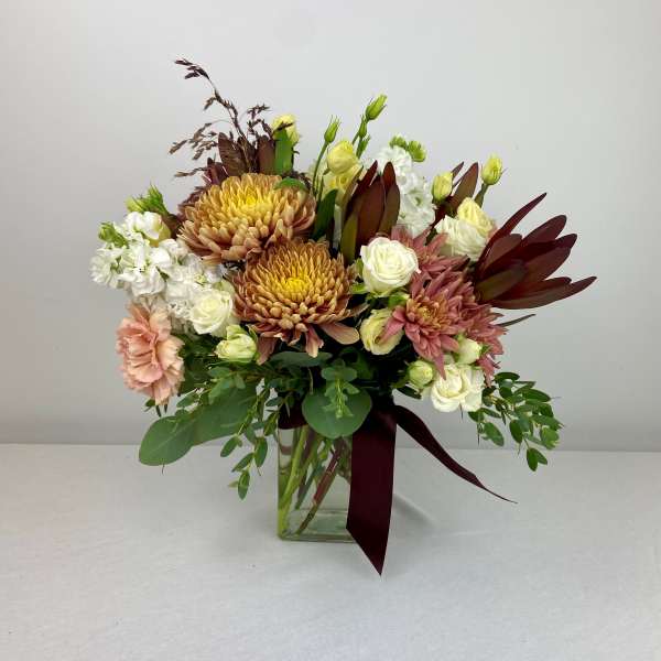 Mixed bouquet of chrysanthemums, roses, and carnations in a glass vase