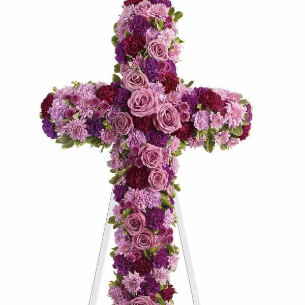 Cross-shaped floral tribute in pink, purple, and burgundy flowers on an easel