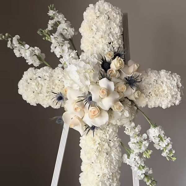 White floral cross on a stand with cream roses and dark accents