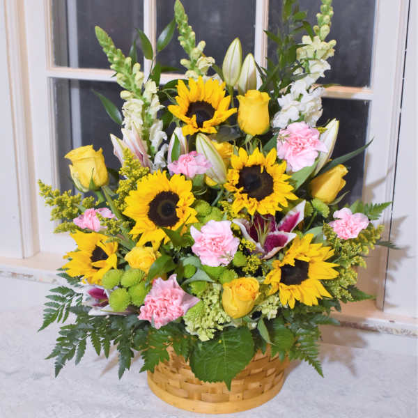 Basket arrangement with sunflowers, yellow roses, and pink carnations