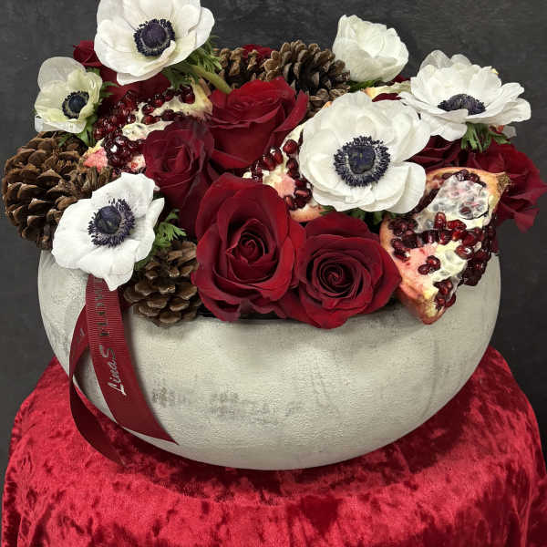 Red roses and white anemones in a round vase with pinecones and pomegranate pieces