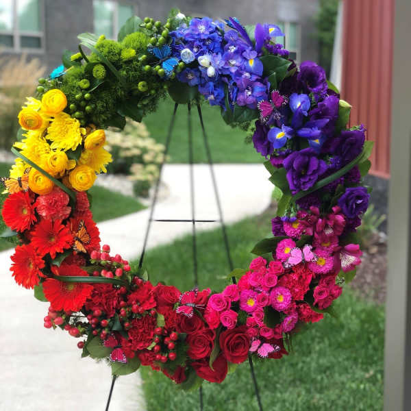 Rainbow floral wreath on a stand with roses, gerbera daisies, and purple blooms
