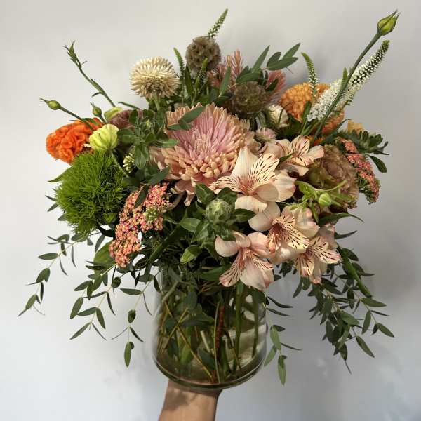 Loose peach and orange mixed flower arrangement with green accents in a clear glass vase