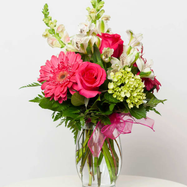 Pink roses and gerbera daisies in a glass vase with a pink ribbon
