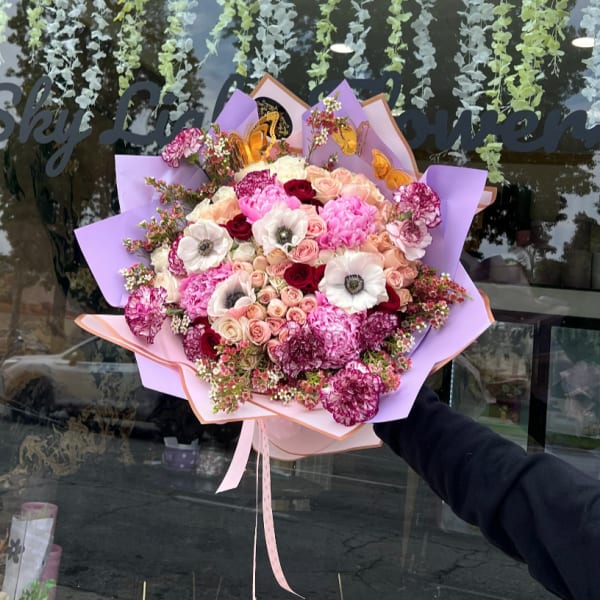 Large bouquet of pink and white flowers wrapped in lavender paper