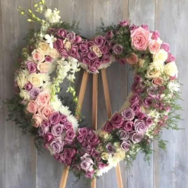 Heart-shaped floral wreath of pink, purple, and white roses on an easel