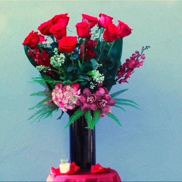 Tall bouquet of red roses and pink orchids in a black vase