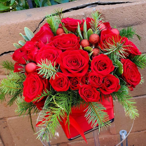 Arrangement of red roses with evergreen sprigs in a red square container
