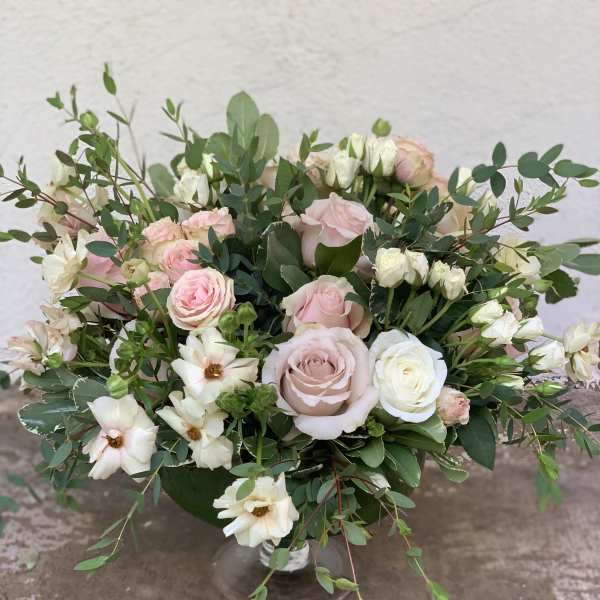 Pink and white roses in a clear glass vase with airy greenery