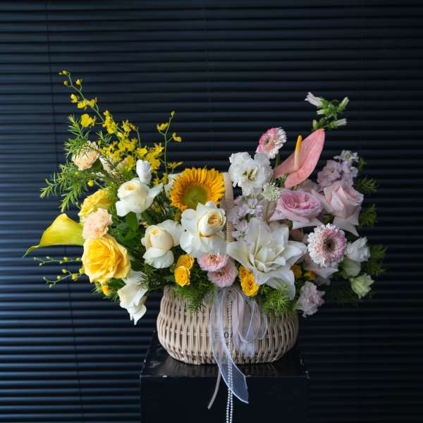 Mixed pastel flower arrangement in a woven basket with ribbon