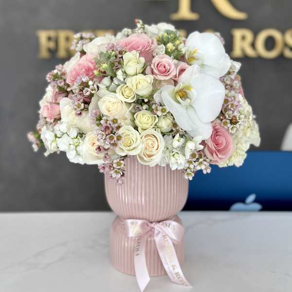 Pink and white rose arrangement in a ribbed pink vase with a ribbon