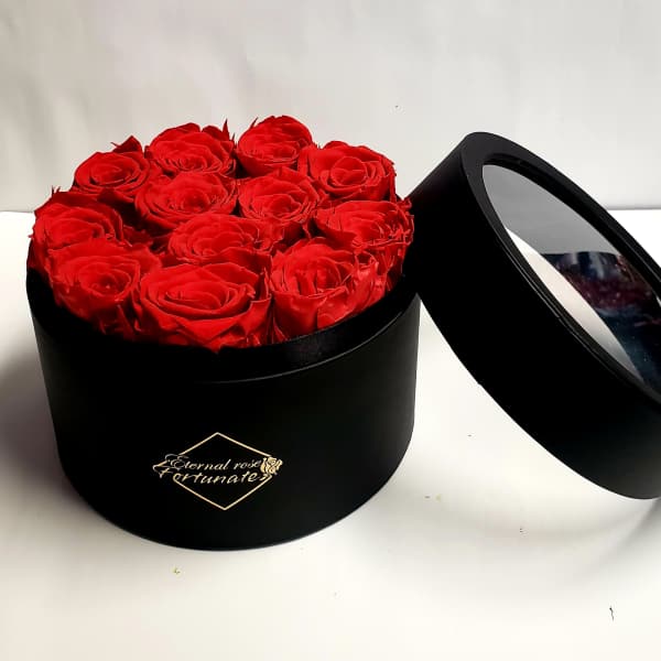 Red roses arranged in a black round box with a clear lid