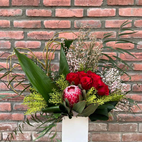 Red roses and a protea in a tall white vase