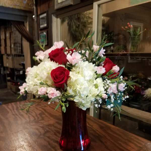 Bouquet of red roses, white hydrangeas, and pink carnations in a red glass vase