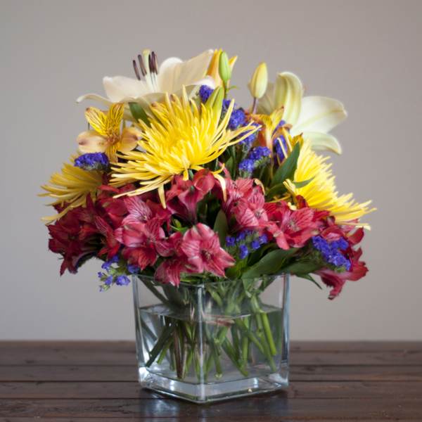 Mixed bouquet of lilies, alstroemeria, and yellow spider mums in a glass vase
