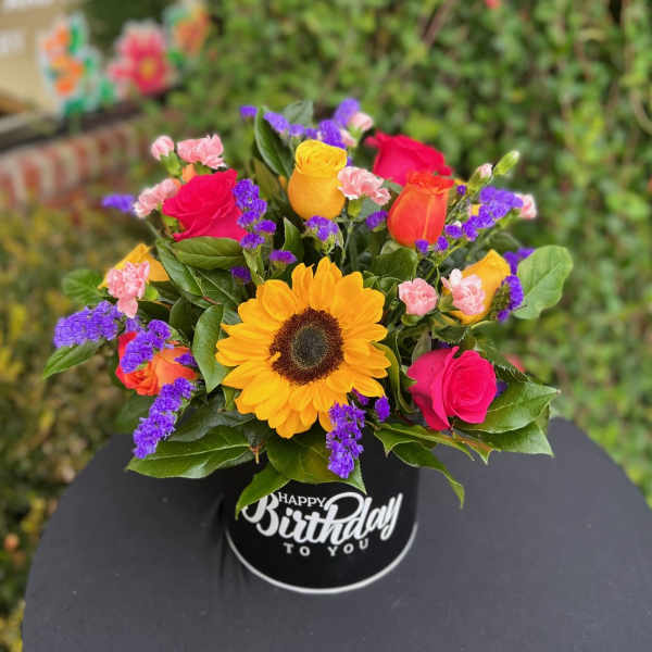 Colorful bouquet with a sunflower and roses in a black birthday container