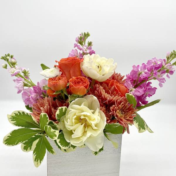 Mixed bouquet of orange, cream, and pink flowers in a white box