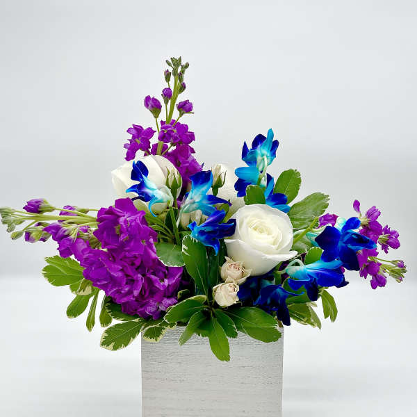 Purple and blue flowers with white roses in a white box
