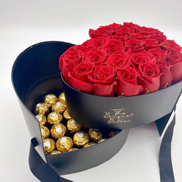 Red roses in a black heart-shaped box with gold-wrapped chocolates