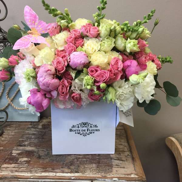 Pink and cream roses arranged in a white box with a pink butterfly accent.