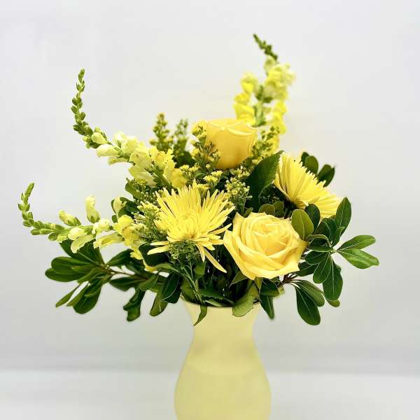 Yellow roses and spider mums in a pale yellow vase