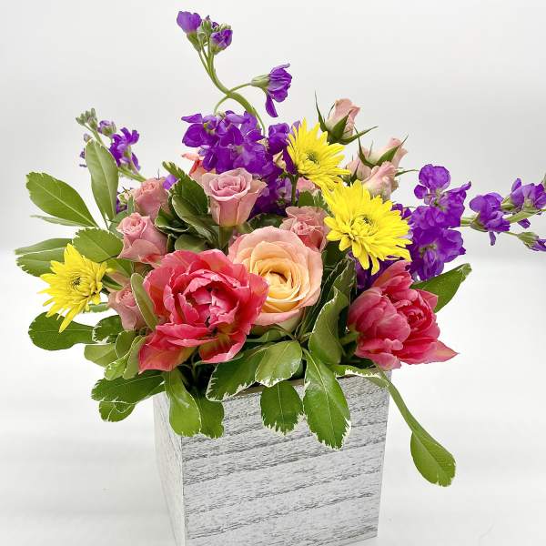Mixed bouquet in a white wooden box with pink, yellow, and purple flowers