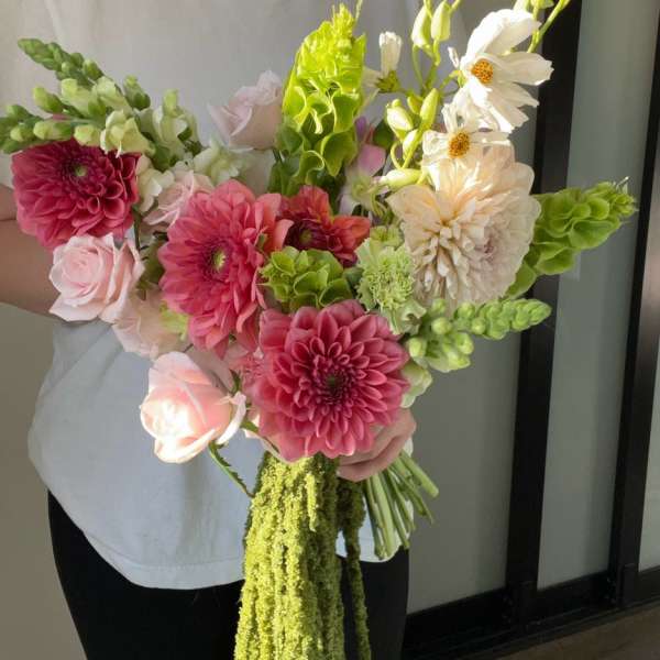 Handheld bouquet of pink, white, and green flowers with trailing greenery