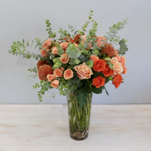 Tall glass vase of peach and orange roses with dahlias and eucalyptus accents