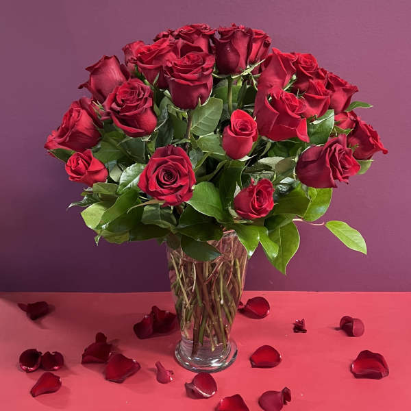 Red roses arranged in a clear glass vase with scattered petals