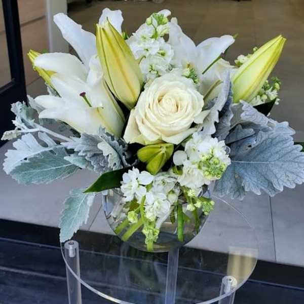White lilies and a rose with silvery foliage in a round glass vase