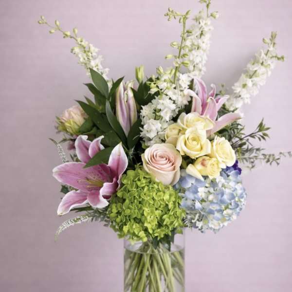 Mixed bouquet of lilies, roses, hydrangea, and white spikes in a glass vase