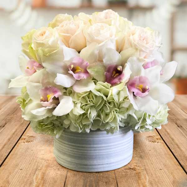 Bouquet of pale roses and orchids in a white container